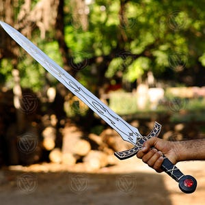 May include: A silver sword with a decorative hilt and blade design. The hilt is black and gold, and the blade features an etched pattern. A red gem is set at the pommel. The sword is held in a hand.