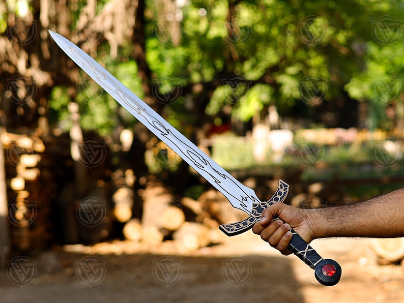 May include: A silver sword with a decorative hilt and blade design. The hilt is black and gold, and the blade features an etched pattern. A red gem is set at the pommel. The sword is held in a hand.