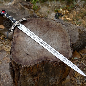 May include: A silver sword with a black handle and a red gem on the pommel rests on a wooden stump. The blade has an intricate design. The sword is a fantasy item.