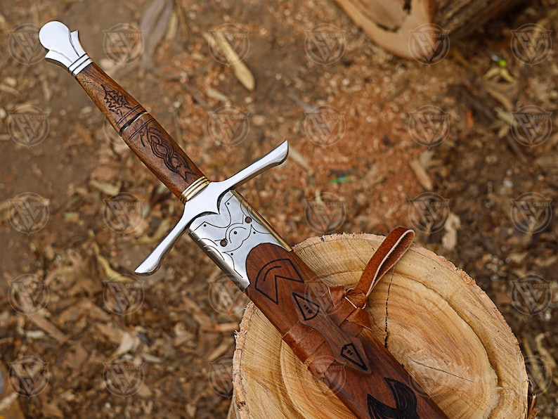 Puede incluir: Una espada de estilo medieval con empu&ntilde;adura de madera y hoja plateada. La empu&ntilde;adura est&aacute; tallada con un patr&oacute;n decorativo. La espada est&aacute; enfundada en una vaina de cuero marr&oacute;n. La espada descansa sobre una superficie de madera.