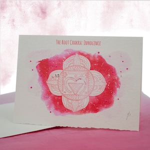 May include: A white card with a red watercolor background and a white mandala design. The text "The Root Chakra: Innocence" is printed at the top of the card.