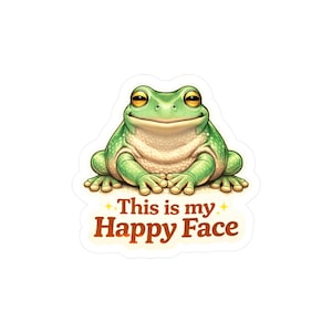 May include: A sticker featuring a smiling green frog with yellow eyes. The frog has a light beige belly and is sitting with its hands clasped. Text on the sticker reads "This is my Happy Face" in brown letters with yellow star accents.