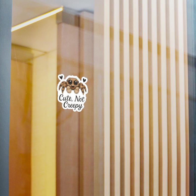 May include: A white sticker with a cartoon spider illustration. The spider has brown and tan fur, large eyes, and a smiling face. The text "Cute, Not Creepy" is below the spider, with two small heart graphics.