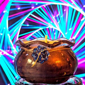 May include: A brown glass candle holder with a yellow candle. The holder has a wavy rim and a blue flower-shaped decoration. The background features a colorful, abstract design with pink, blue, and white lines.