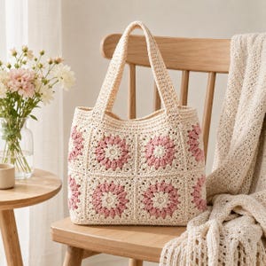Puede incluir: Bolso tote de crochet color crema con cuadrados florales rosas. El bolso tiene dos asas y est&aacute; sobre una silla de madera. Una manta de crochet color crema est&aacute; sobre el respaldo de la silla. Un jarr&oacute;n con flores est&aacute; en una mesa auxiliar.