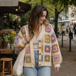 May include: Cream-colored crochet cardigan with colorful square patterns. The cardigan has a V-neck, long sleeves, and wooden buttons. The squares feature shades of pink, purple, blue, yellow, and green. The person is wearing blue jeans and carrying a cream-colored tote bag.