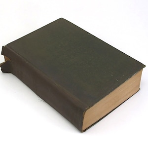 Op de afbeelding: Een donkergroen hardback boek met een versleten leren omslag en een licht beschadigde rug.