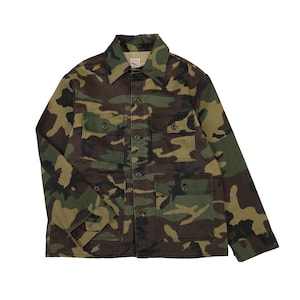 May include: Camouflage pattern jacket with four front pockets and button closures. The jacket features a collared neckline and long sleeves. The color palette includes shades of green, brown, and black.