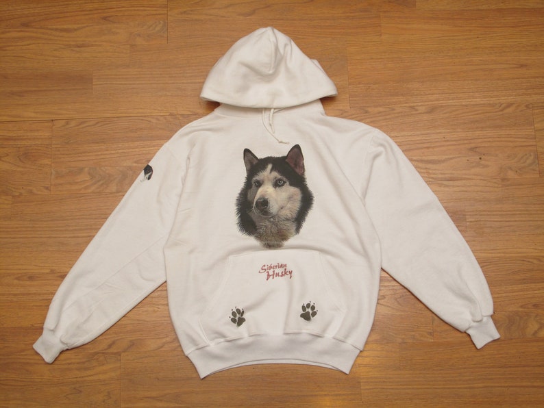 May include: White hoodie featuring a Siberian Husky dog portrait on the front. The design includes the text "Siberian Husky" in red script below the dog's image, and paw prints on the front pocket. A small dog image is on the left sleeve.