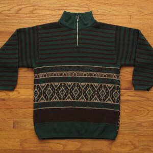 May include: A green and brown sweater with a half-zip collar. The sweater features horizontal stripes on the sleeves and upper chest, with a patterned design of diamonds and geometric shapes across the midsection. The sweater is made of a knitted material.