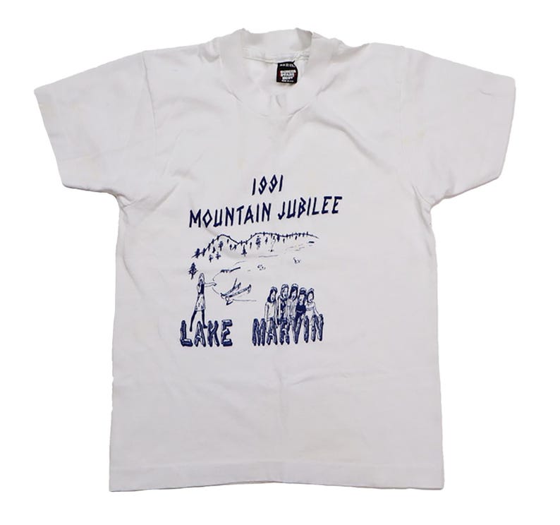 May include: White t-shirt with a blue graphic print of a mountain scene and the text "1991 Mountain Jubilee Lake Marvin".