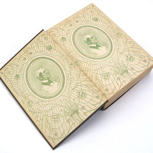 Op de afbeelding: Een open boek met een groene en witte bedrukte omslag. De omslag heeft een cirkelvormig ontwerp met een portret van een man in het midden. Het boek is open op een pagina met een vergelijkbaar ontwerp.