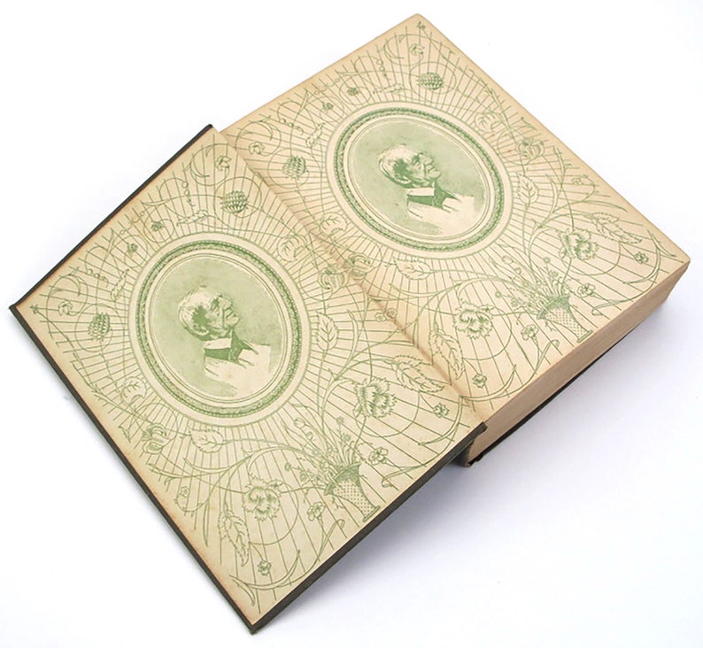 Op de afbeelding: Een open boek met een groene en witte bedrukte omslag. De omslag heeft een cirkelvormig ontwerp met een portret van een man in het midden. Het boek is open op een pagina met een vergelijkbaar ontwerp.