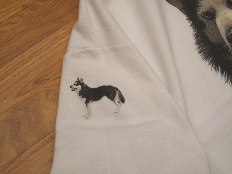 May include: White sweatshirt featuring a detailed illustration of a husky dog on the sleeve. The dog is depicted in black, white, and gray, with a realistic style. The design is on a plain white background.