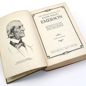 Op de afbeelding: Een open boek met een zwart-witte illustratie van Ralph Waldo Emerson op de linkerpagina. De rechterpagina heeft de titel "The Complete Writings of Ralph Waldo Emerson" en de tekst "Containing all of his inspiring Essays, Lectures, Poems, Addresses, Studies, Biographical Sketches and Miscellaneous Works. Complete in One Volume. Wm. H. Wise & Co., Publishers, New York."