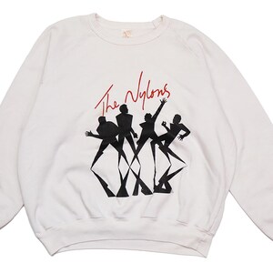 May include: White long-sleeve sweatshirt with a black and white graphic of a band called "The Nylons".