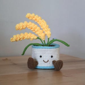 Planta de cebada hecha a mano con ganchillo en una maceta sonriente.
