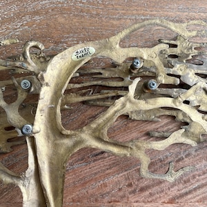 K&ouml;nnte beinhalten: Eine baumf&ouml;rmige Skulptur aus messingfarbenem Metall mit strukturierter Oberfl&auml;che. Der Baum hat komplizierte &Auml;ste und ist mit Schrauben befestigt. Ein kleines Etikett tr&auml;gt die Aufschrift "BAKED ENAMEL".