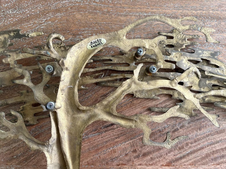 K&ouml;nnte beinhalten: Eine baumf&ouml;rmige Skulptur aus messingfarbenem Metall mit strukturierter Oberfl&auml;che. Der Baum hat komplizierte &Auml;ste und ist mit Schrauben befestigt. Ein kleines Etikett tr&auml;gt die Aufschrift "BAKED ENAMEL".