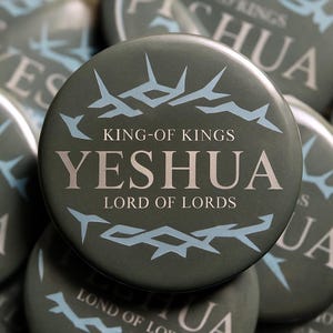 May include: A collection of round, olive-green buttons with the text "YESHUA, LORD OF LORDS" in silver lettering. The buttons also feature a light blue crown of thorns design and the words "KING-OF KINGS".