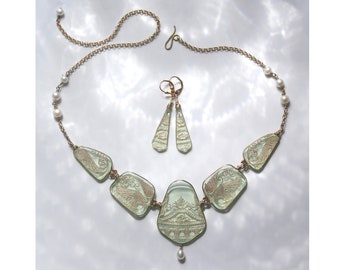 May include: A delicate green glass necklace with gold accents and a pearl pendant. The necklace is made up of five pieces of glass, each with a different design. The necklace is paired with matching earrings.