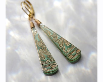 May include: A pair of dangle earrings with a green, teardrop-shaped pendant. The pendant has a gold-colored, intricate design.