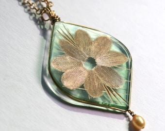 May include: A gold chain necklace with a green glass pendant featuring a gold flower design. The pendant has a small pearl hanging from the bottom.