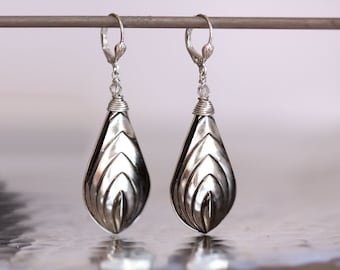 May include: A pair of silver teardrop earrings with a geometric design and a crystal accent.