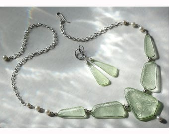 May include: A jewelry set featuring a necklace, earrings, and bracelet. The necklace and bracelet are made of silver chain and small pearls. The necklace has several light green, rectangular, and patterned pendants. The earrings are light green, elongated, and teardrop-shaped.