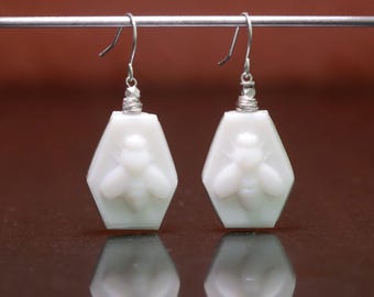 May include: White ceramic earrings shaped like a honeycomb with a bee design.
