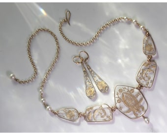 May include: A gold necklace with a clear glass pendant featuring a floral design. The necklace is accented with small white pearls and includes matching earrings with a similar design.