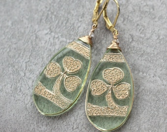 May include: A pair of green glass earrings with gold shamrock designs. The earrings are teardrop shaped and have gold wire wrapped around the top.