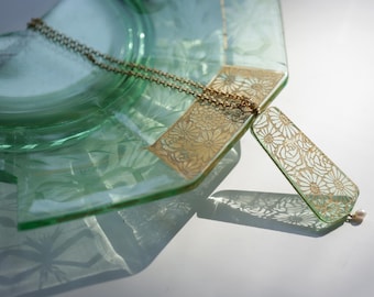 May include: A gold necklace with a delicate chain and a pendant featuring a floral design. The pendant is made of clear glass with a gold overlay and a pearl accent.