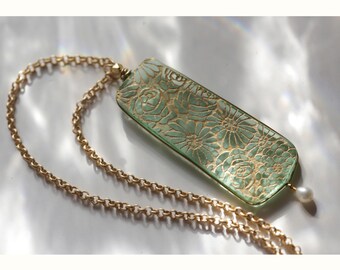 May include: A green glass pendant necklace with a gold floral design and a single pearl accent. The necklace has a gold chain.