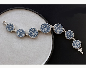May include: A silver bracelet with blue and white ceramic round beads. The beads have a floral pattern.