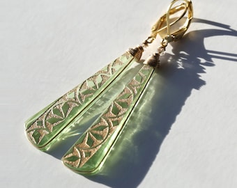 May include: A pair of green glass earrings with gold geometric designs. The earrings are dangle style and have a gold hook closure.