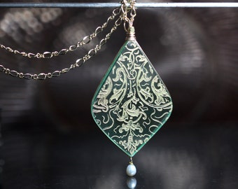 May include: A gold chain necklace with a green glass pendant featuring a gold filigree design. The pendant is shaped like a teardrop and has a single pearl hanging from the bottom.
