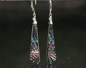 May include: A pair of long, teardrop-shaped dangle earrings featuring a metallic, iridescent finish with shifting hues of purple, green, and blue. The surface displays a geometric, embossed pattern, and each earring hangs from a silver-toned leverback.