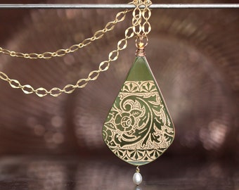 May include: A gold chain necklace with a green teardrop pendant featuring an intricate floral design. The pendant has a small pearl hanging from the bottom.