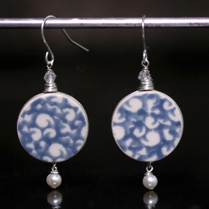 May include: A pair of silver earrings with blue and white porcelain round pendants and a single pearl dangling from each.