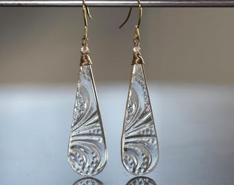 May include: A pair of teardrop-shaped earrings with a clear, textured design. The earrings have gold-colored hooks and are accented with small beads and wrapped wire. The design features a floral pattern.