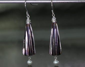 May include: A pair of silver earrings with a teardrop-shaped pendant. The pendants are iridescent and have a textured surface. Each pendant is accented with a small pearl.