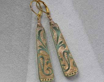 May include: A pair of long, green and gold earrings with a floral design. The earrings are made of metal and have a hook closure.