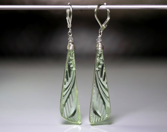 May include: A pair of light green, Art Deco-style earrings. Each earring features a long, triangular, etched glass pendant with a floral design. The pendants are suspended from silver-colored lever-back ear wires and wrapped wire detailing.