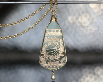 May include: A gold chain necklace with a green glass pendant featuring a gold etched floral design and a single pearl hanging from the bottom.