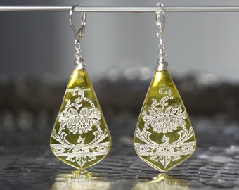 May include: A pair of teardrop-shaped earrings with a silver wire wrap and a yellow glass teardrop pendant. The pendant has a silver floral design etched into it.