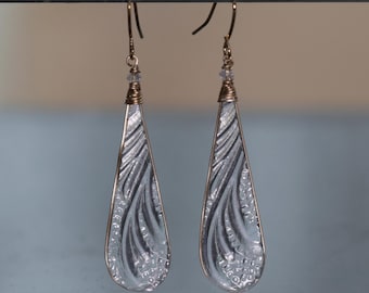 May include: A pair of silver-colored teardrop earrings with a textured, etched design. The earrings have gold-colored wire accents and ear hooks. The design features a flowing, organic pattern.