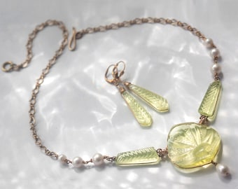 May include: A delicate gold chain necklace with a green carved pendant and pearl accents. Matching earrings with green carved drops.