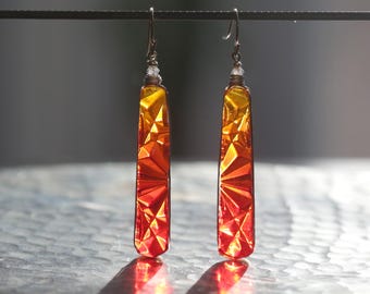 May include: A pair of long, rectangular earrings with a gradient of yellow, orange, and red glass. The glass is faceted and has a geometric pattern.