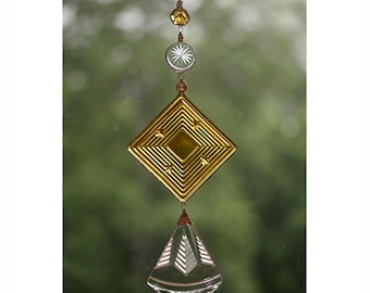 May include: A gold and clear glass suncatcher with a diamond shape and a teardrop shape hanging from it. The suncatcher has a beaded chain with a small round bead at the top.